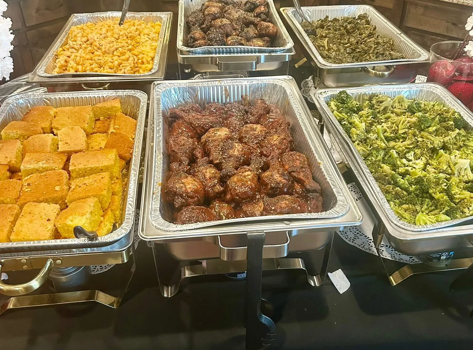 Chafing trays of mac and cheese, barbecue chicken, collard greens, cornbread, and broccoli on a catering buffet