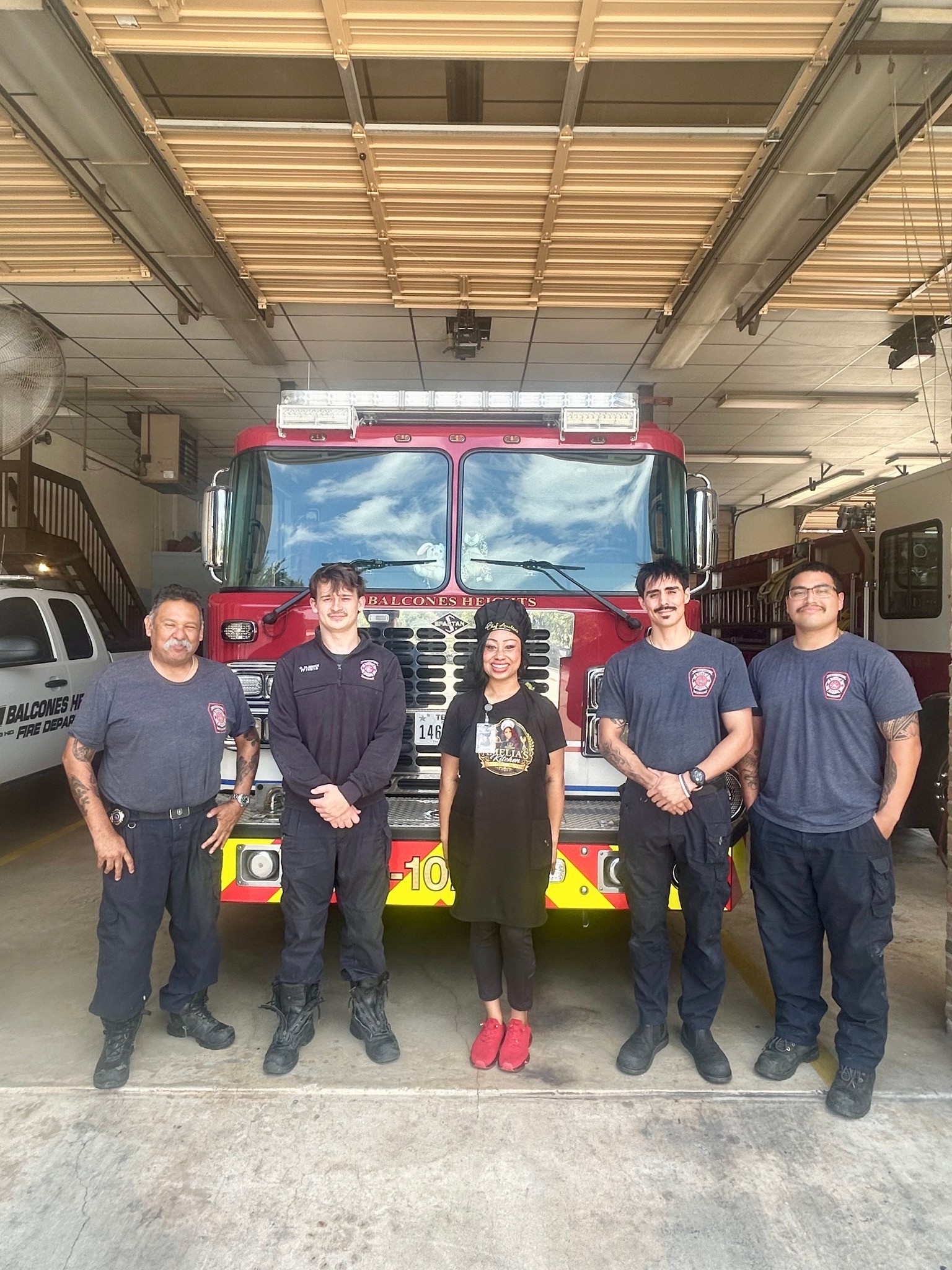 Chef Amelia stands with four uniformed Balcones Heights firefighters in front of a fire engine.