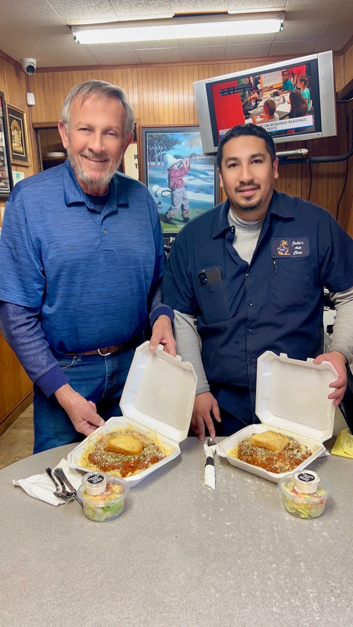 Two people holding takeout meal containers inside a local auto shop
