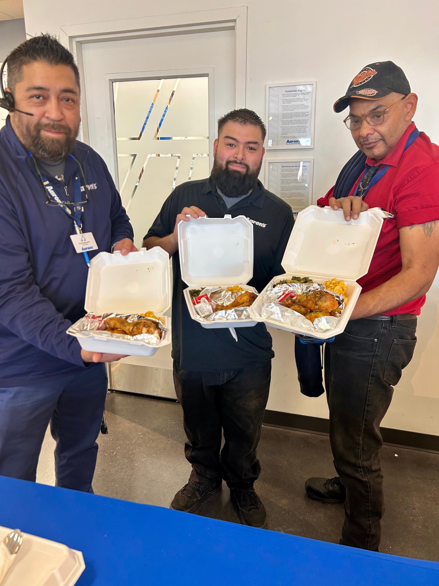 Three Aaron’s team members hold open takeout meals during a catered workplace event.