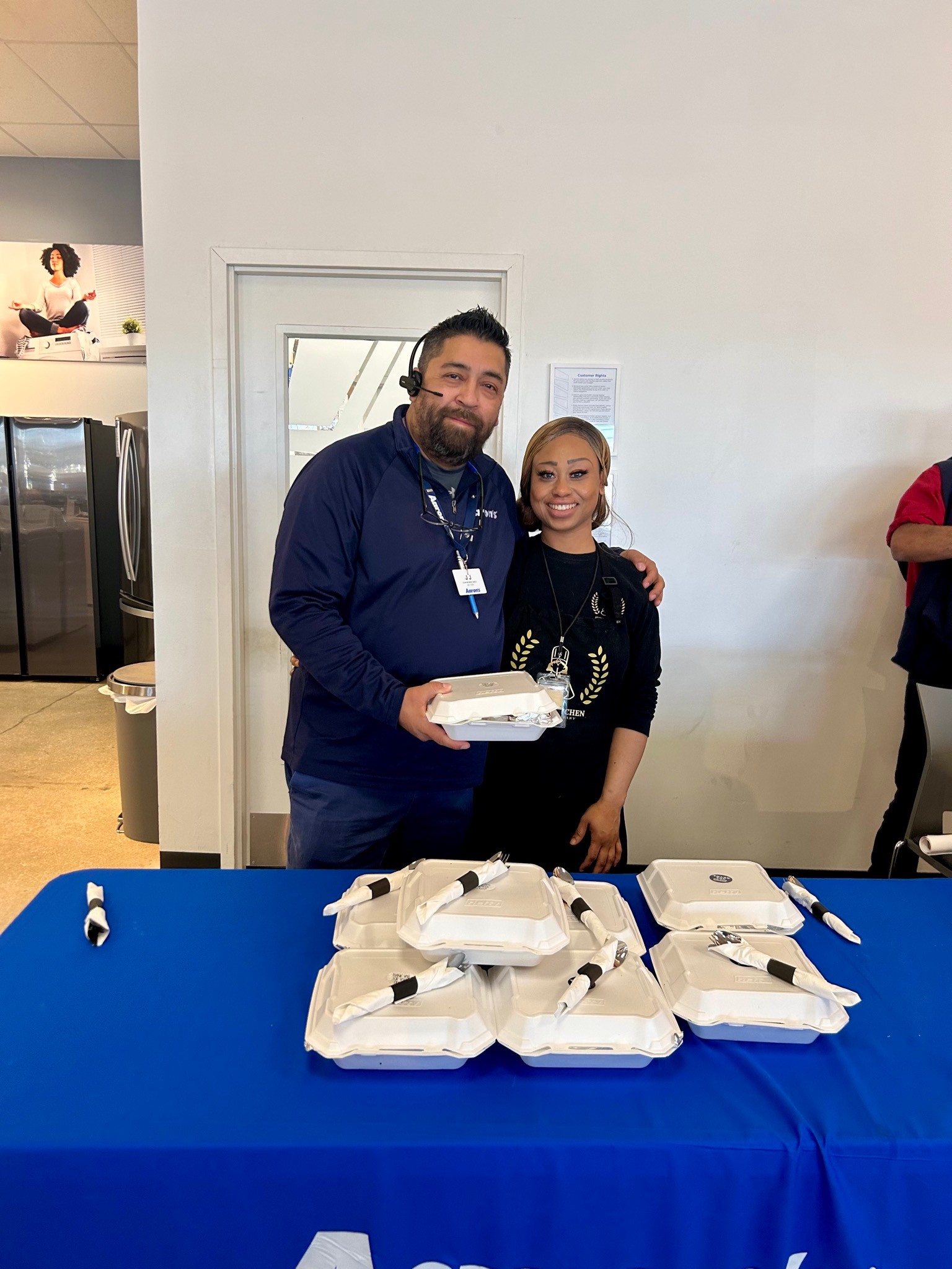 Chef Amelia stands with an Aaron’s team member behind a table of boxed catered meals.
