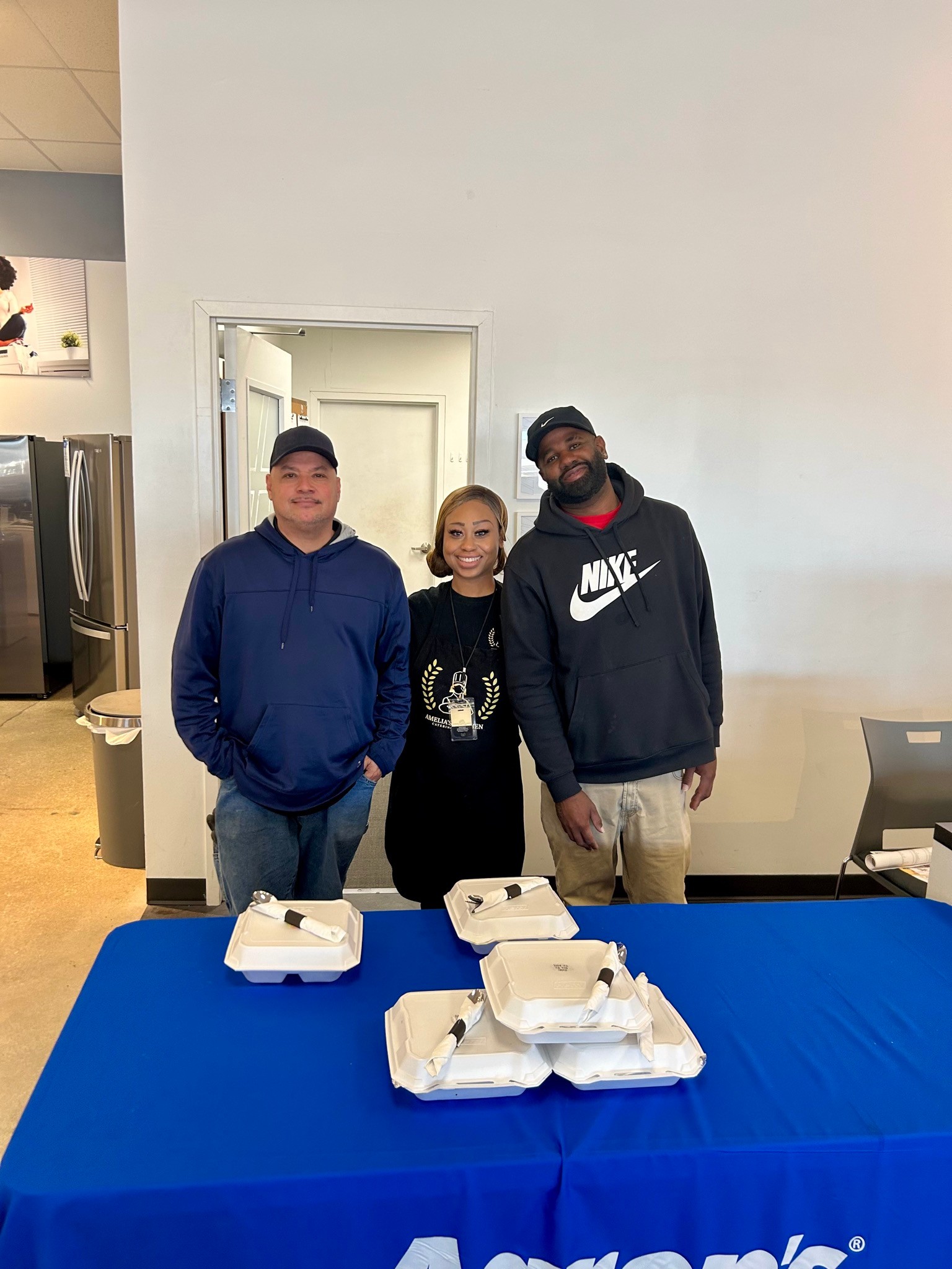 Chef Amelia stands with two Aaron’s team members behind a table of boxed catered meals.