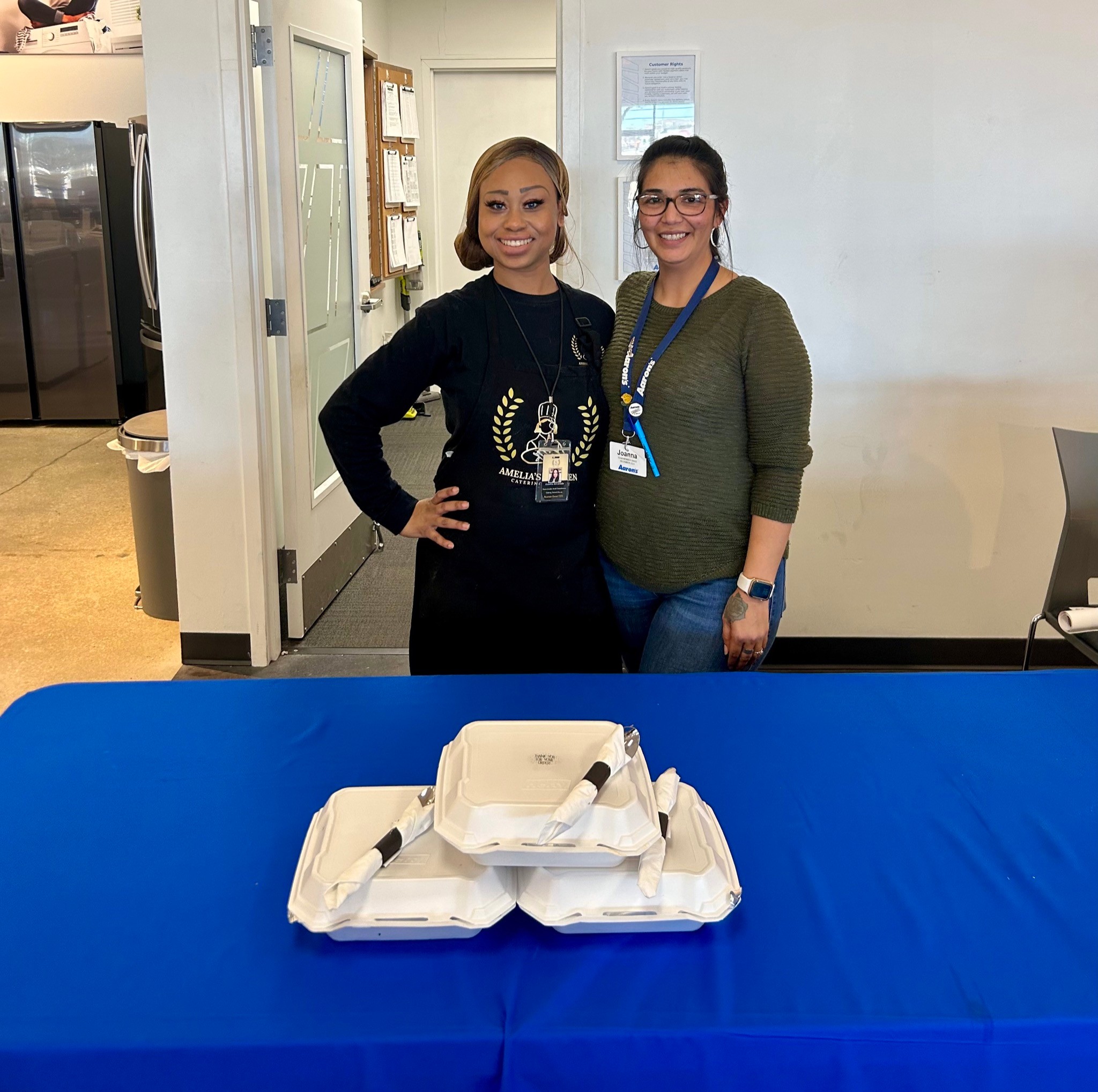 Chef Amelia stands with an Aaron’s team member behind a table of boxed catered meals.