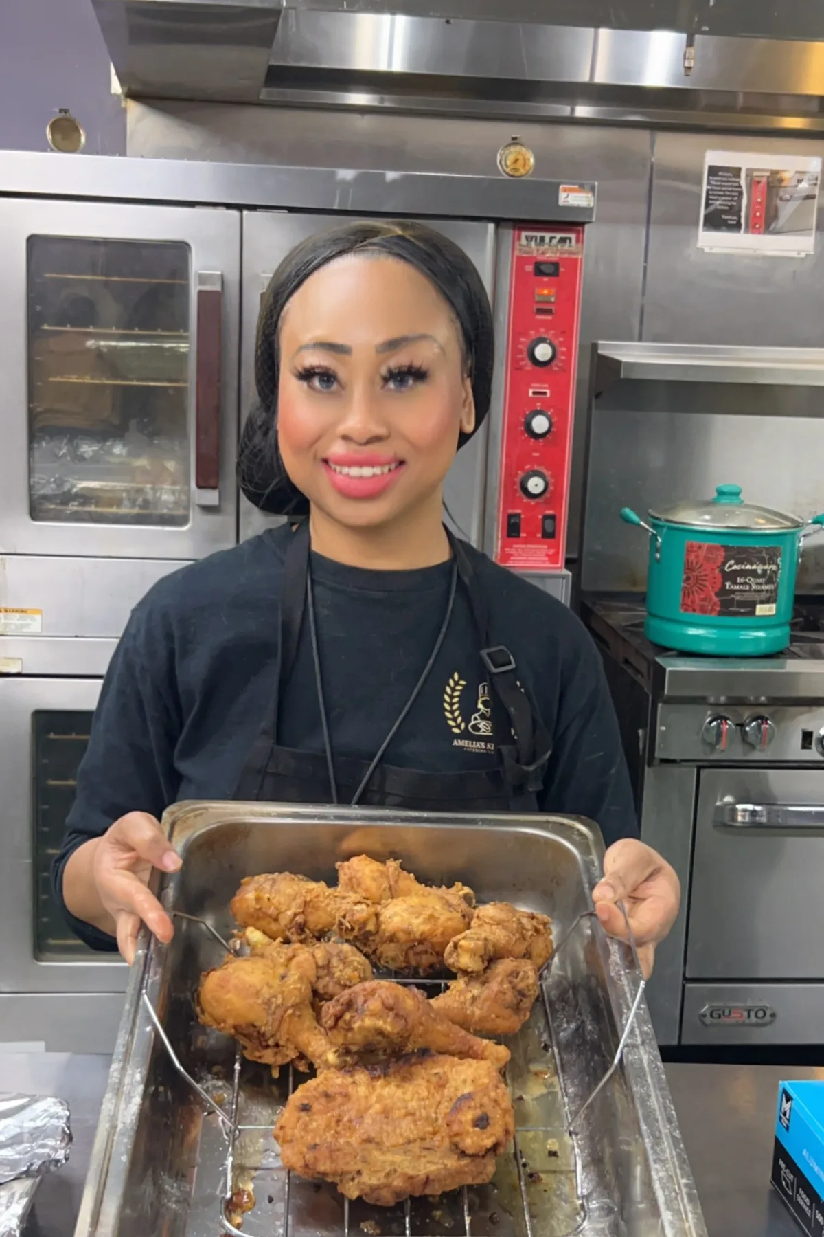 Chef Amelia holding a tray of freshly fried chicken beside the ovens in her commercial kitchen