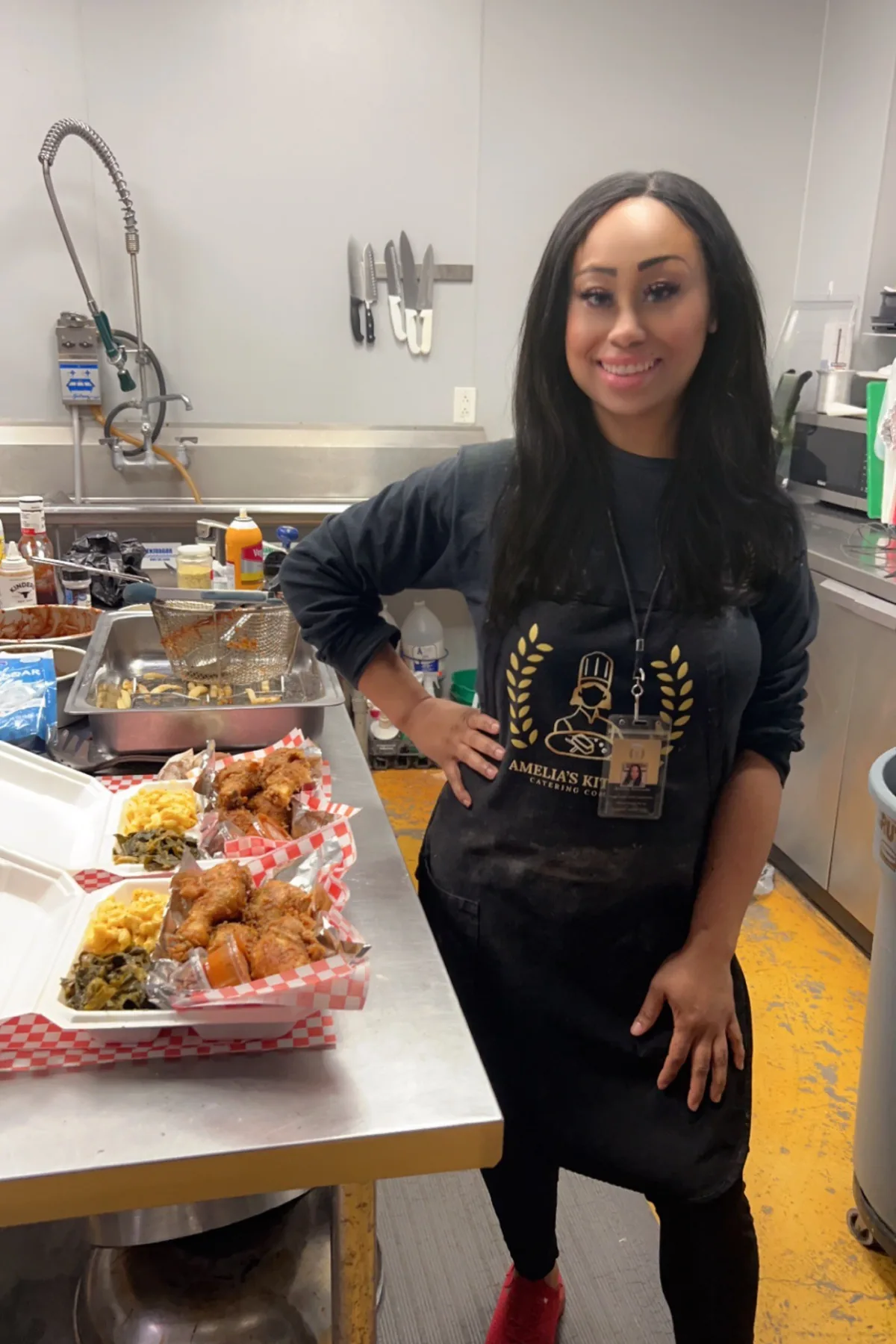 Chef Amelia standing beside the fryer and wall knife rack in her commercial kitchen
