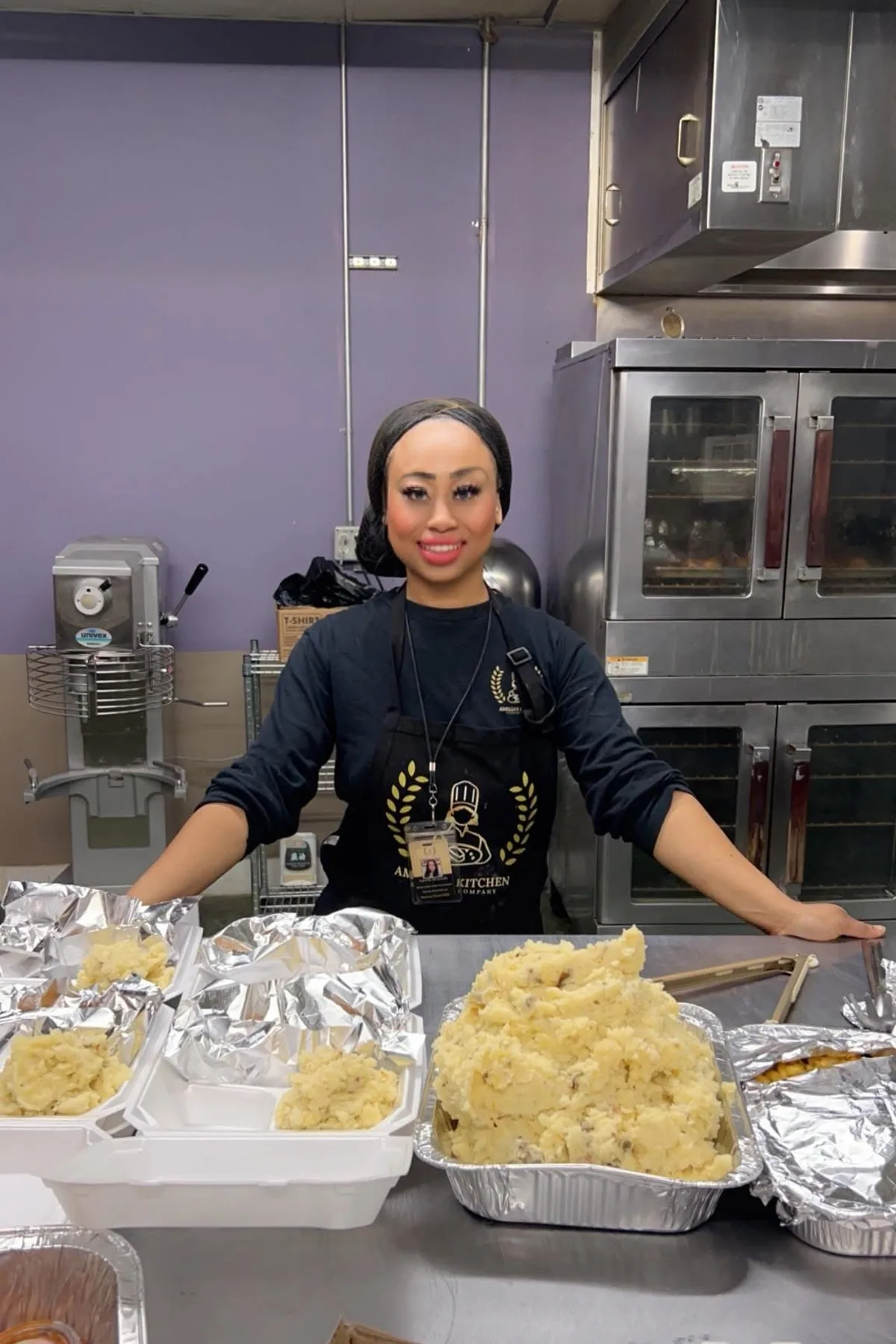 Chef Amelia standing behind a prep table of freshly made mashed potatoes in her commercial kitchen