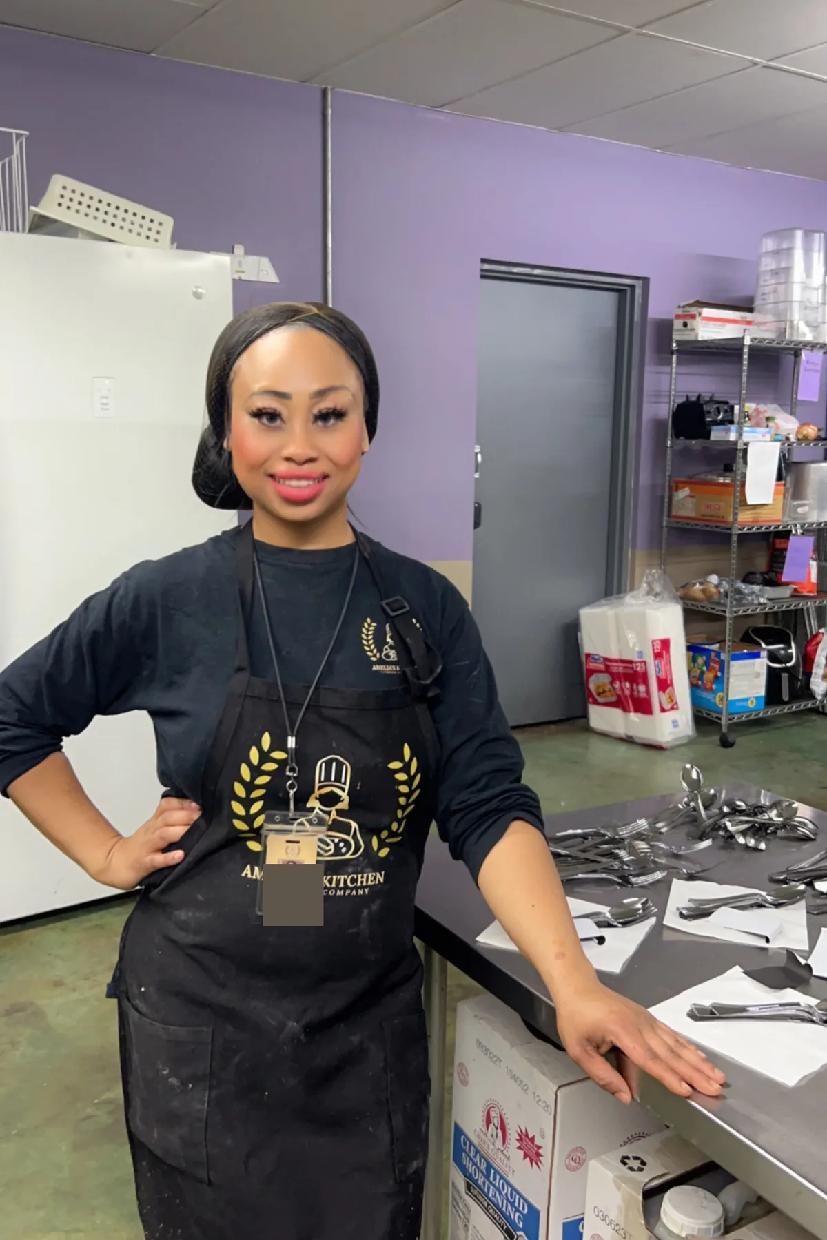 Chef Amelia standing beside a rolled-silverware station in her commercial kitchen