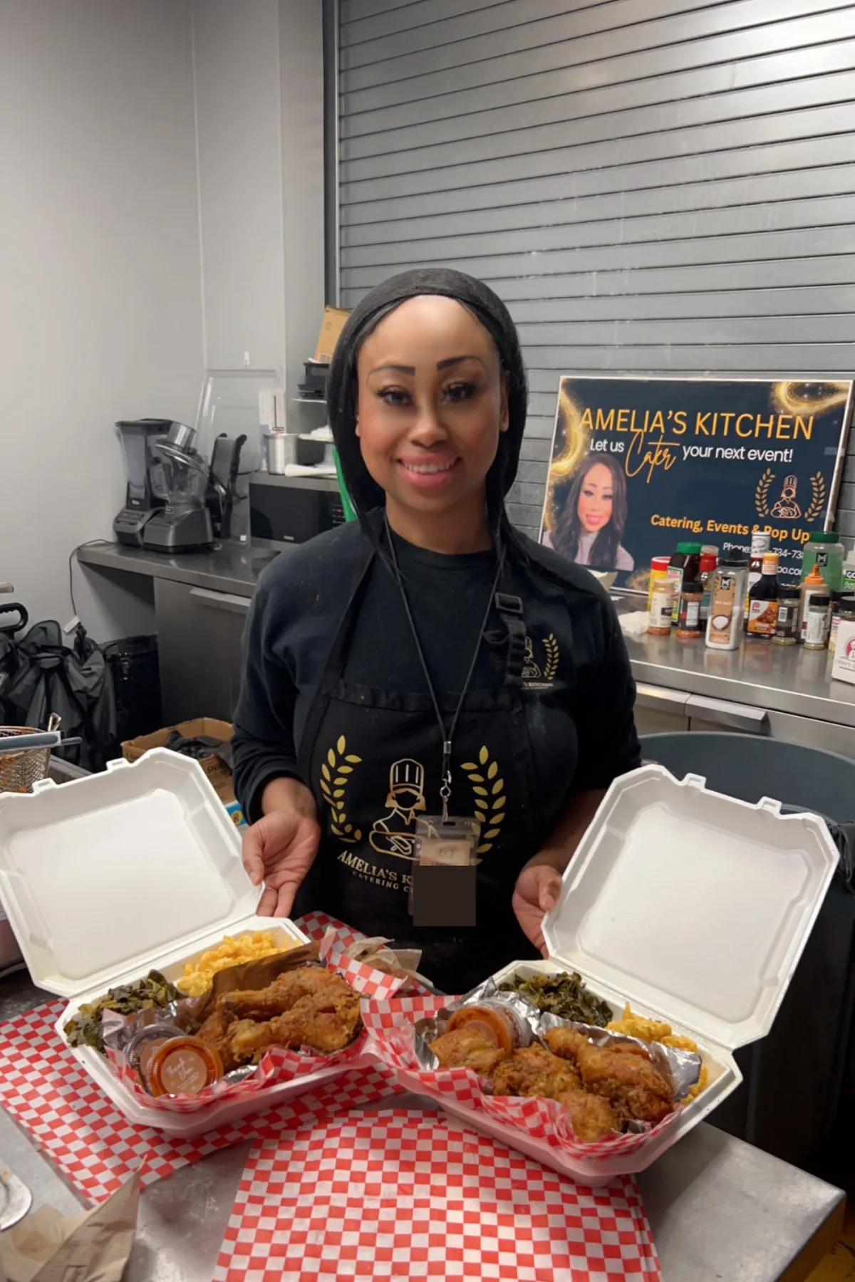 Chef Amelia holding two open containers of fried chicken, greens, and sides in her commercial kitchen